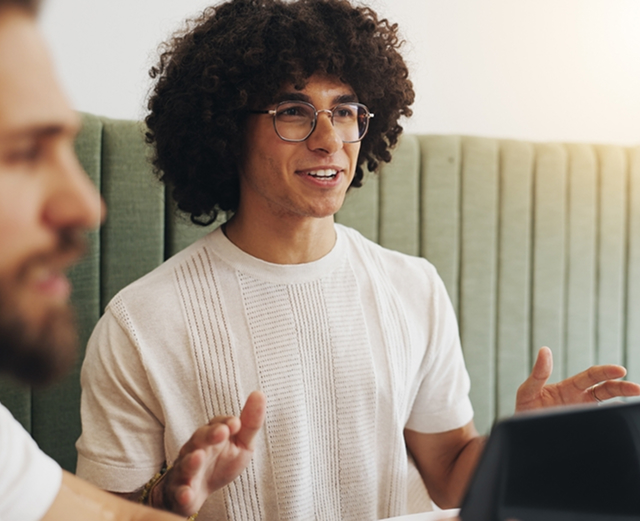 Person speaking in a meeting, wearing glasses.