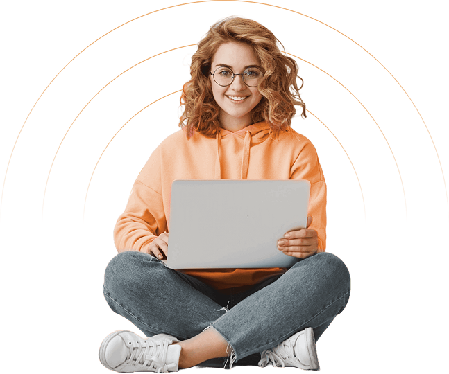 Smiling person using laptop, seated cross-legged.